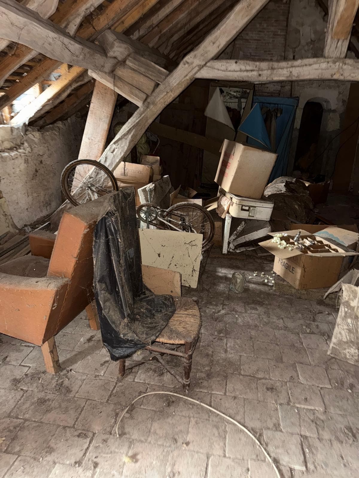 Grenier sous charpente encombré de meubles anciens, vélo et cartons avant débarras