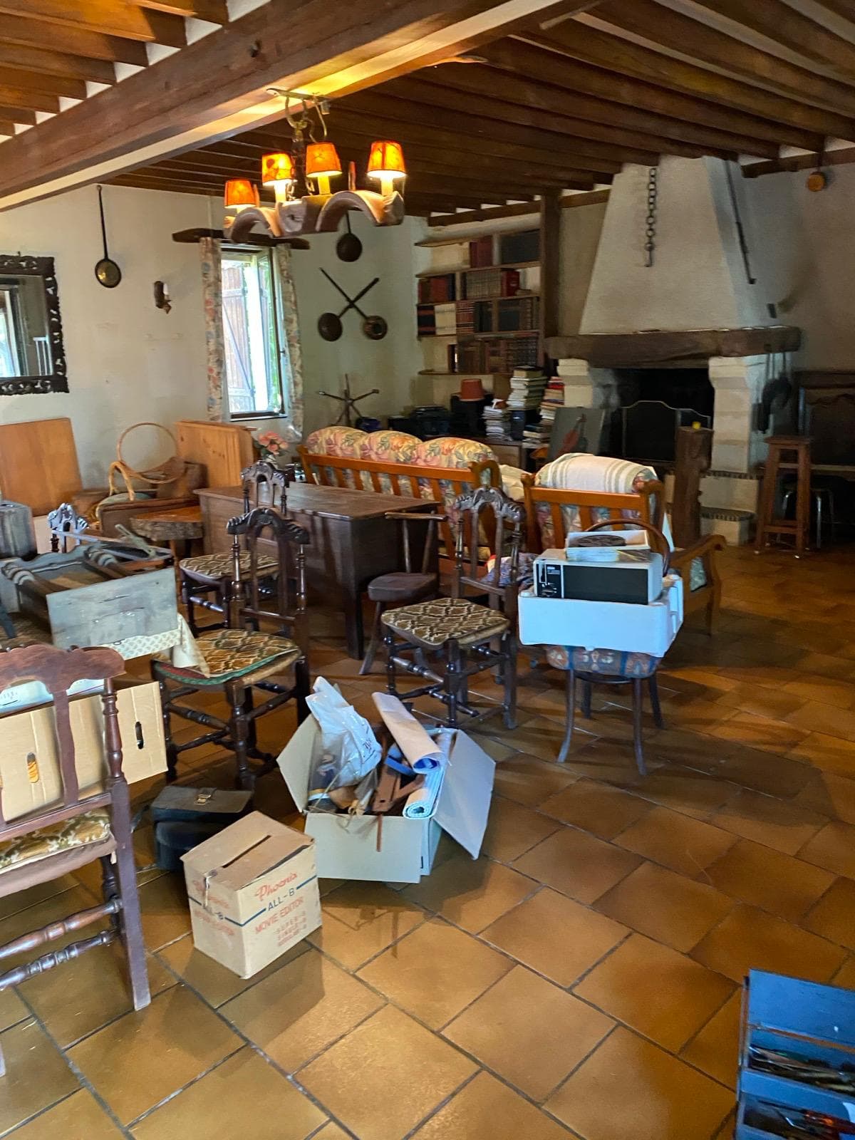 Séjour encombré de meubles, cartons et électroménager avant intervention